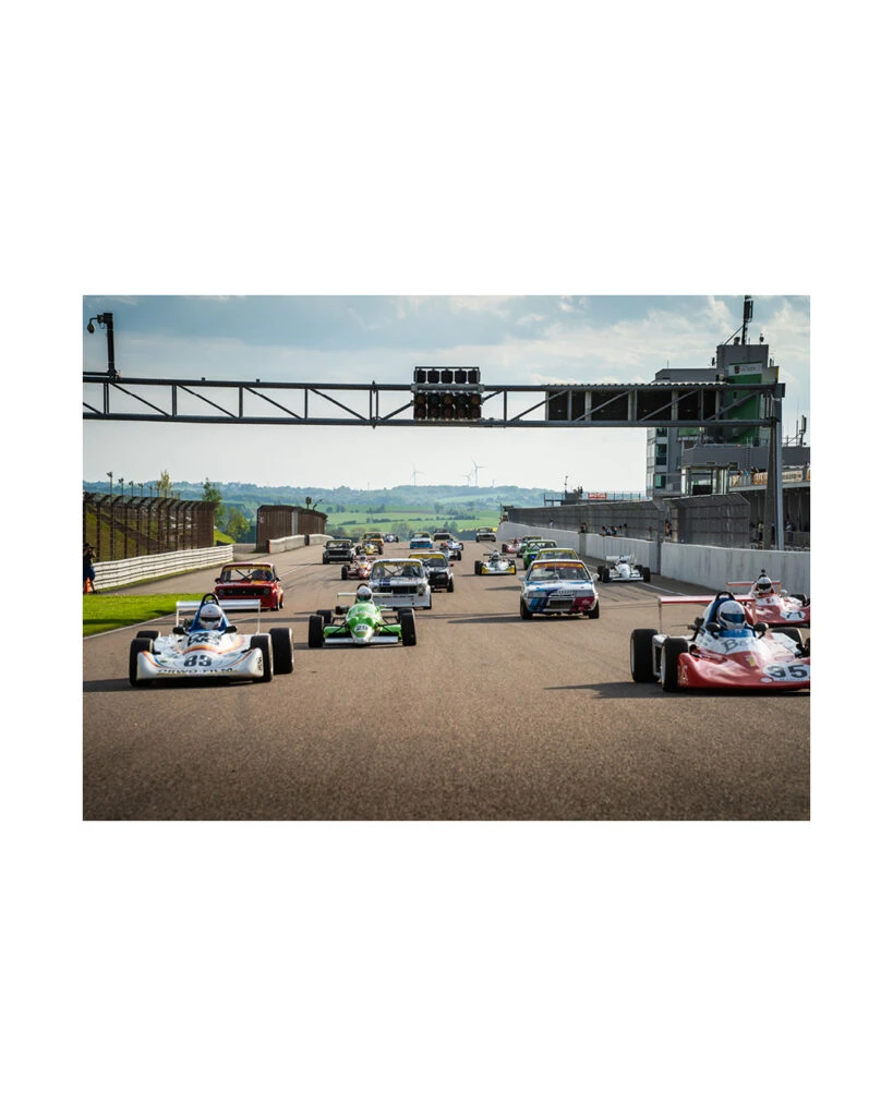 Startfeld des ADAC Historic Cup OST mit historischen Formel- und Tourenwagen auf der Start-Ziel-Geraden des Sachsenrings unter der Ampelbrücke.