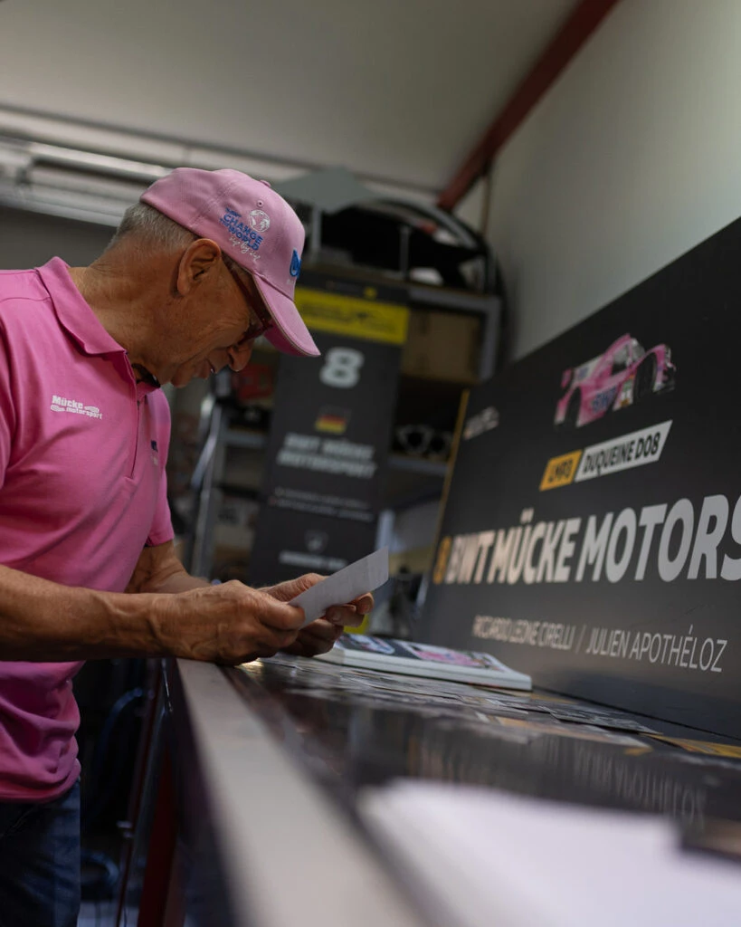 Peter Mücke von Mücke Motorsport beugt sich über einen Tisch und betrachtet historische Fotos aus seiner Karriere.