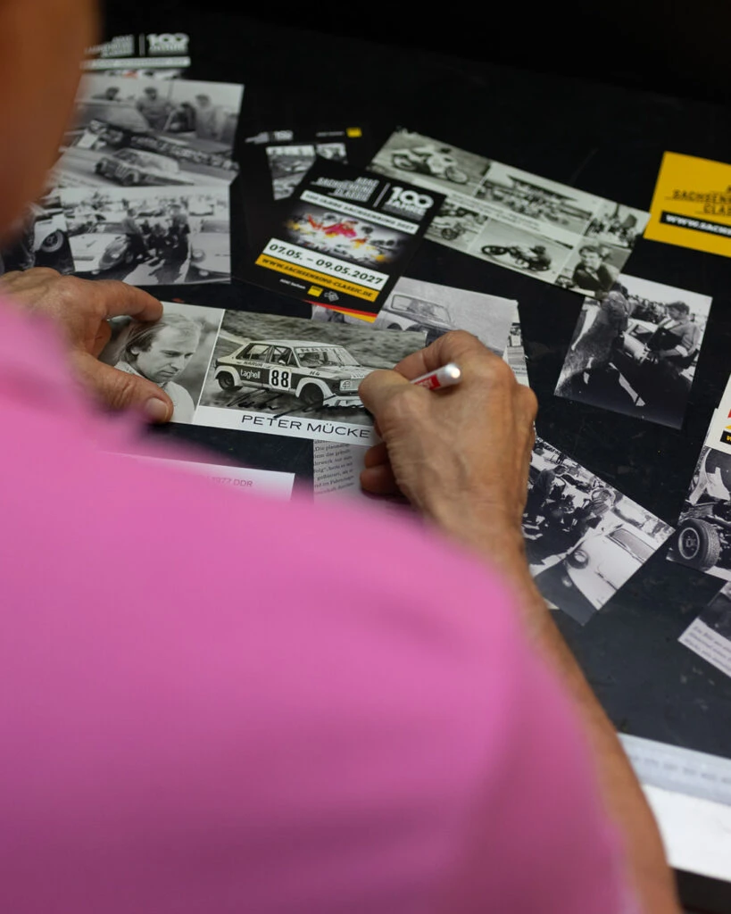 Draufsicht: Peter Mücke unterschreibt ein altes Schwarz-Weiß-Foto aus seinen Rennfahrer-Zeiten mit einem Stift.
