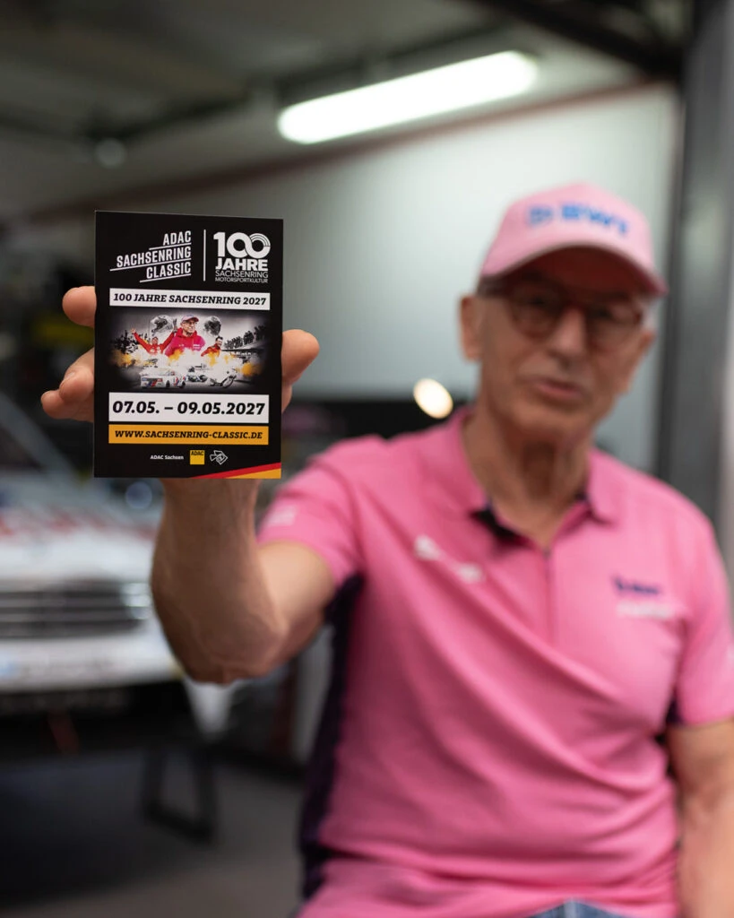 Peter Mücke hält eine Einladungskarte für das Motorsport-Event Sachsenring Classic in die Kamera.