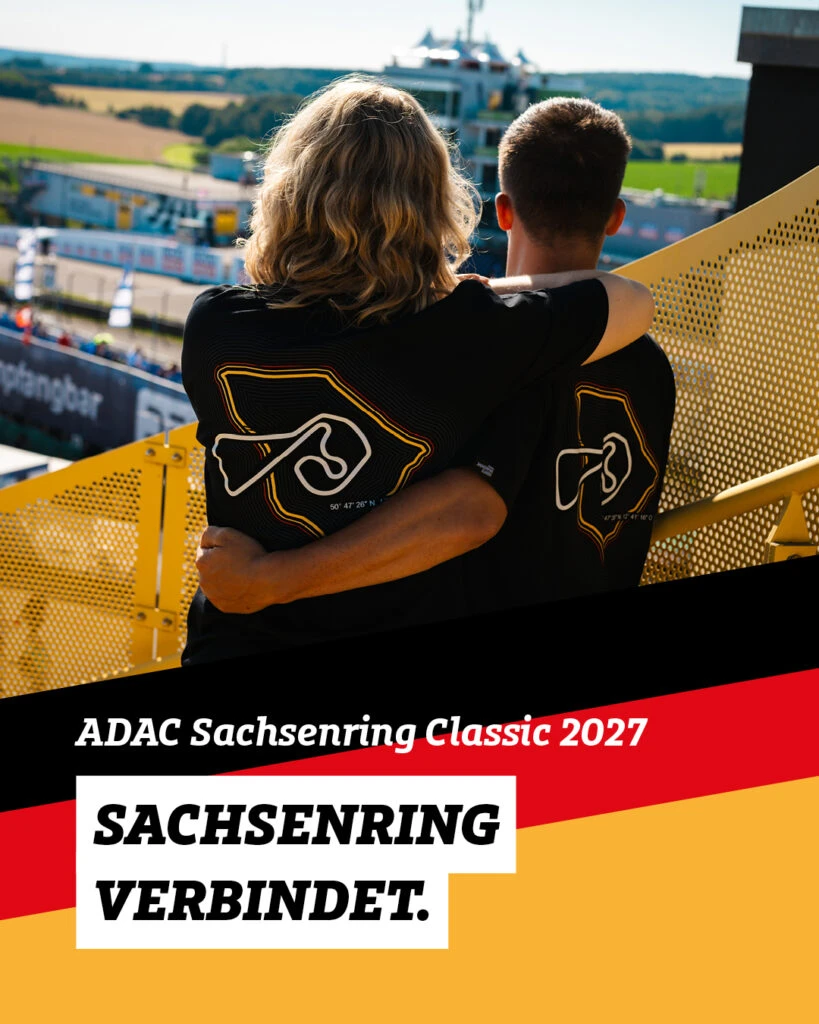 Zwei Personen umarmen sich von hinten auf einer gelben Tribüne und blicken gemeinsam auf eine Rennstrecke. Beide tragen schwarze T-Shirts mit einer stilisierten Streckengrafik des Sachsenrings auf dem Rücken. Im unteren Bereich des Bildes befinden sich ein schwarzer Schriftzug „ADAC Sachsenring Classic 2027“ sowie die Worte „SACHSENRING VERBINDET.“ in schwarzen Großbuchstaben auf weißem Grund vor dem Hintergrund der deutschen Nationalfarben Schwarz, Rot und Gold.