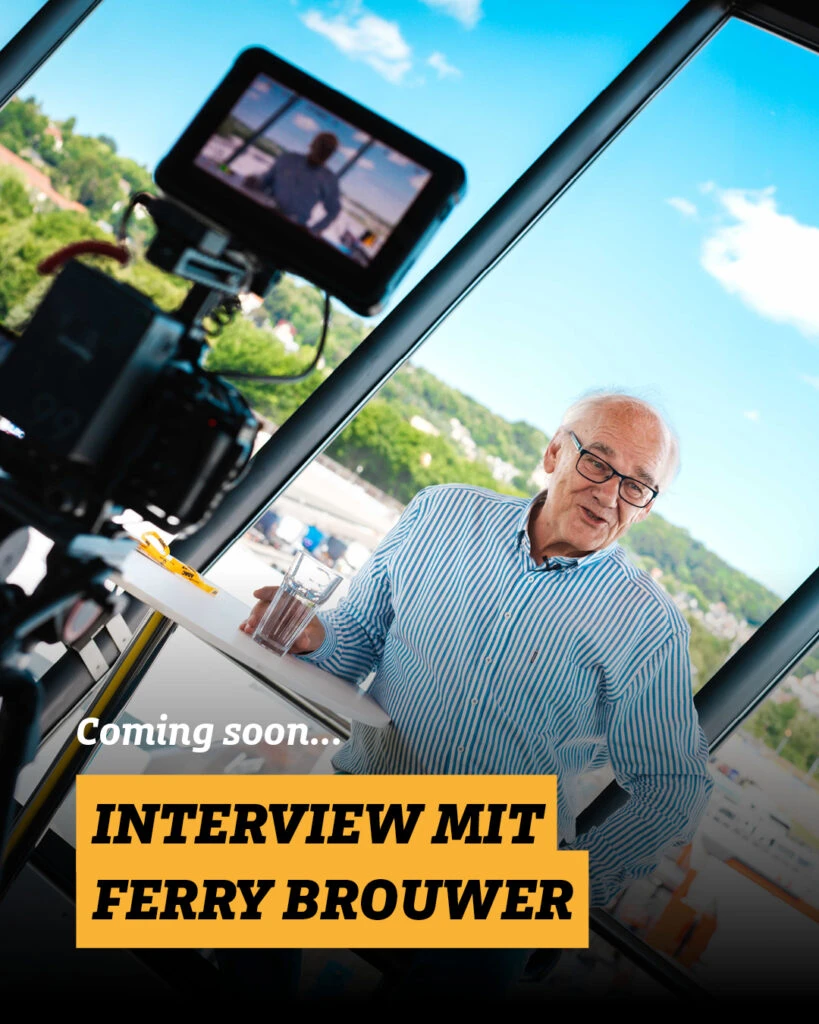 Ankündigung für ein Video-Interview mit Ferry Brouwer vor einer Kamera bei Aufnahmen im Studio
